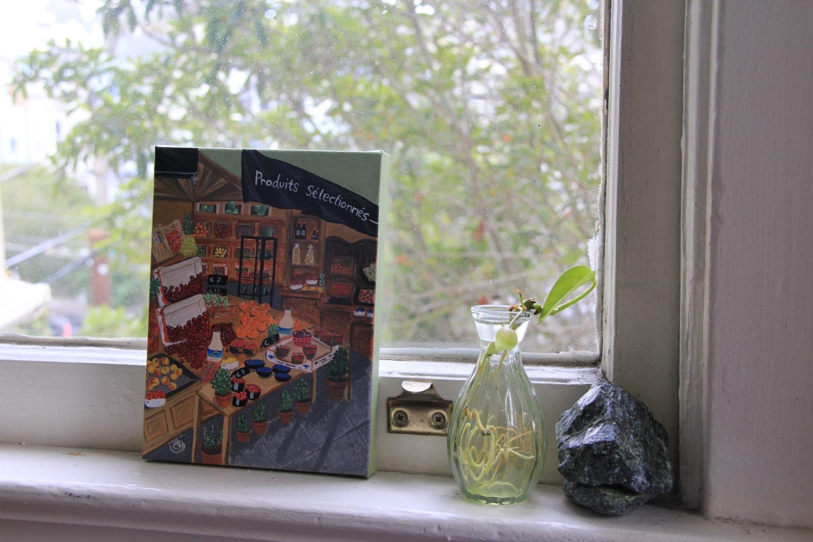 One of Korin's paintings on a sunny windowsill beside a small glass vase and a stone